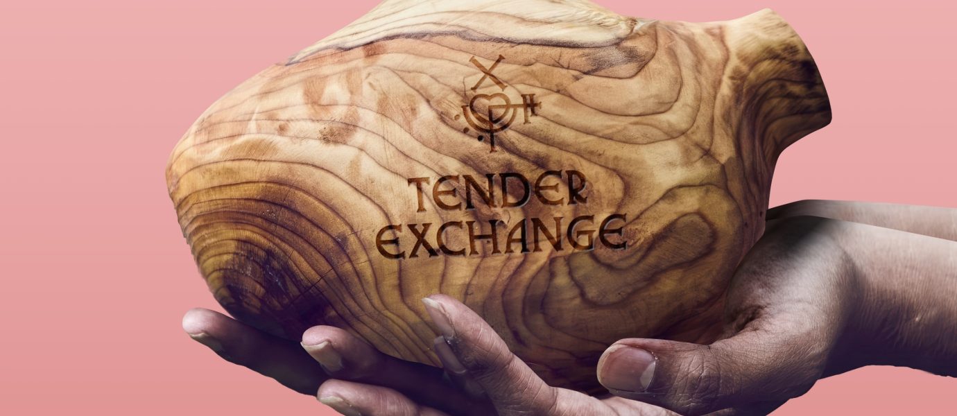 A pair of hands gently holds a wooden vessel engraved with a symbol and the words TENDER EXCHANGE against a pink gradient background.