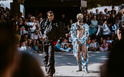 Two male dancers one in black leather, the other in blue frills parade and vogue infront of an outdoor audience on a sunny day in Barcelona