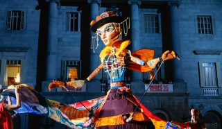 A giant bee puppet at nightime in Barcelona with a ribbon skirt held out in a twirl