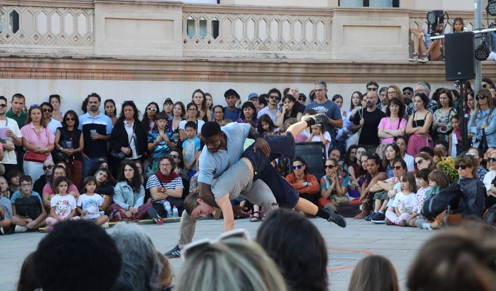 Two dancers perform an acrobatic move in front of a crowd of people.