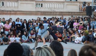 Two dancers perform an acrobatic move in front of a crowd of people.
