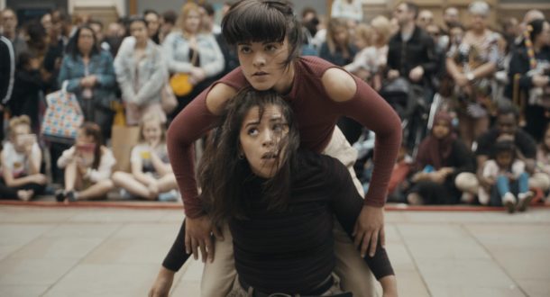 Two female dancers balancing on each others backs in an outdoor performance