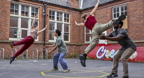 Two male and two female dancers in casual wear 'play' in a school playground