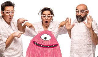 Three adults in white textured shirts and white glasses look surprised and point at a pink, one-eyed cartoon monster with a big smile, standing in front of them against a white background.