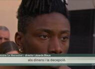 A close-up of a person with dark skin and short dreadlocks, wearing a gold earring, looking serious. Catalan text on screen reads: els diners i la decepció..